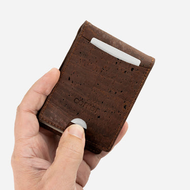 Hand holding a brown cork wallet with a visible brand logo on a light gray background
#color_brown